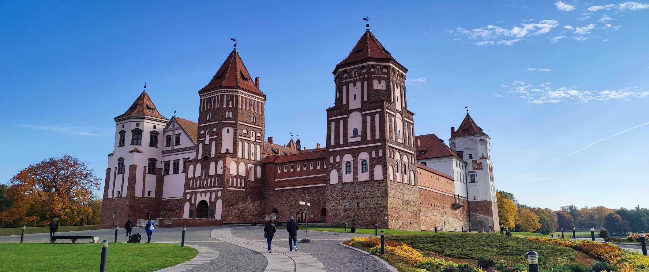 People walking up a sloping path leading to Mir Castle, an imposing red brick castle in Belarus
