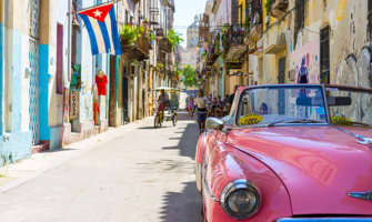 a classic pink car on the colorful streets of Havana, with a Cuban flag in the background