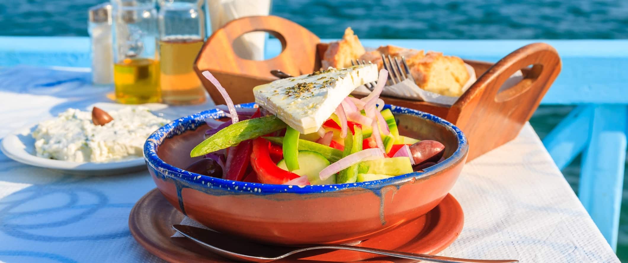 Greek salad, olive oil, bread, and dip at a table by the ocean in Greece