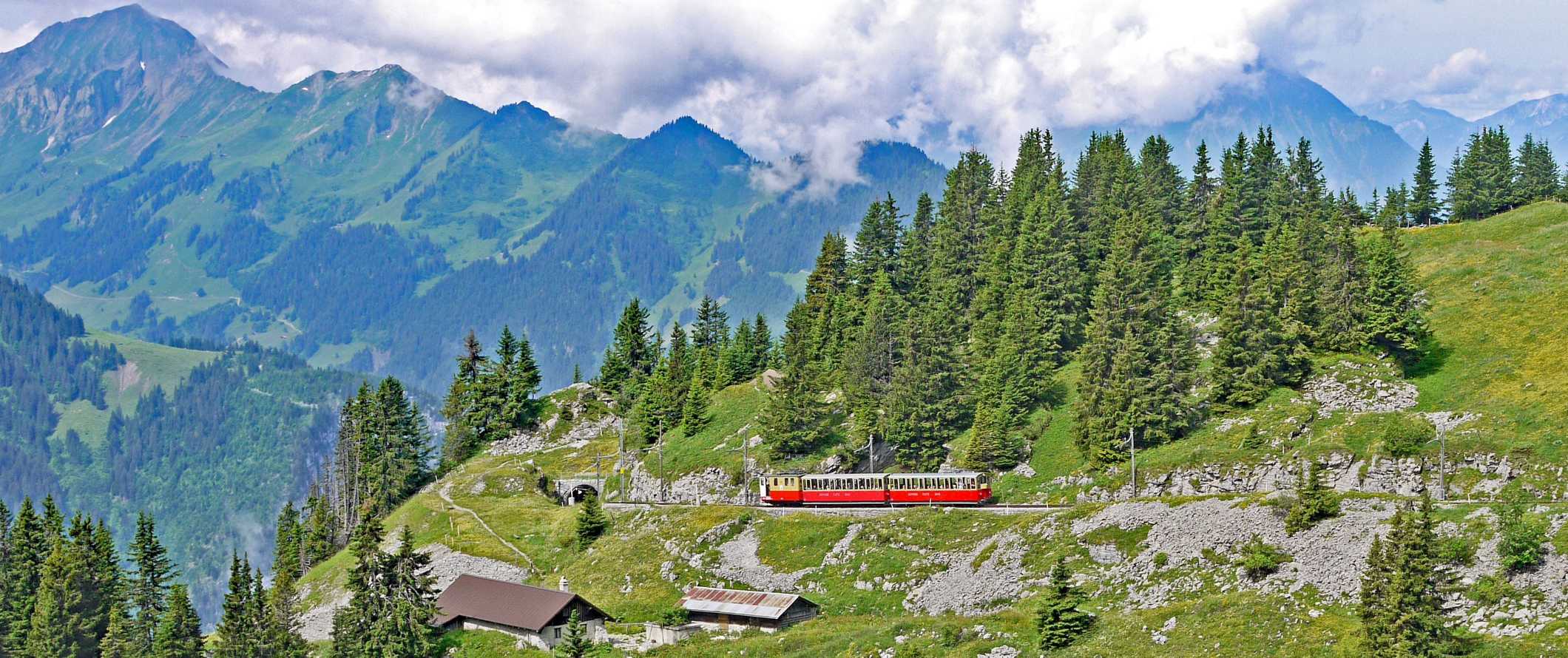 Red train climbing a dramatic incline with sharp mountain peaks in the background on the Jungfraujoch Railway in Interlaken, Switzerland