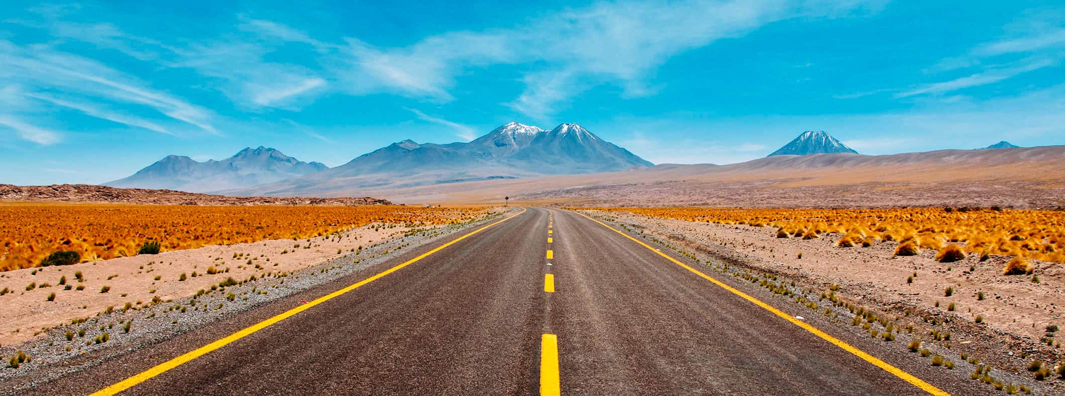 A wide open road in the desert with a bright blue sky and mountains in the distance