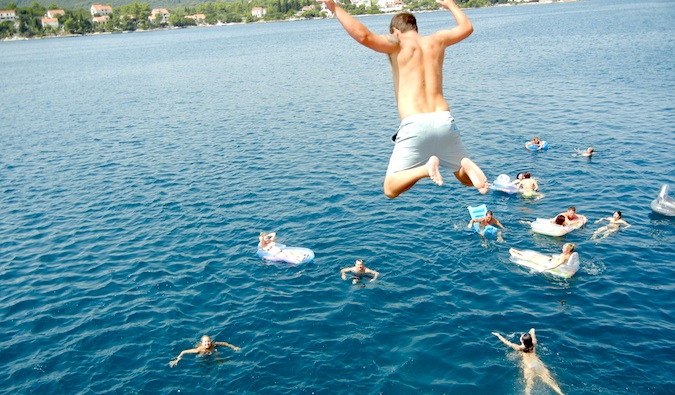 A person jumping into the water from a cliff as they travel the world