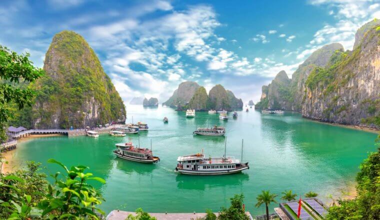 Boats in the calm waters of Ha Long Bay near Hanoi, Vietnam surrounded by tall mountains