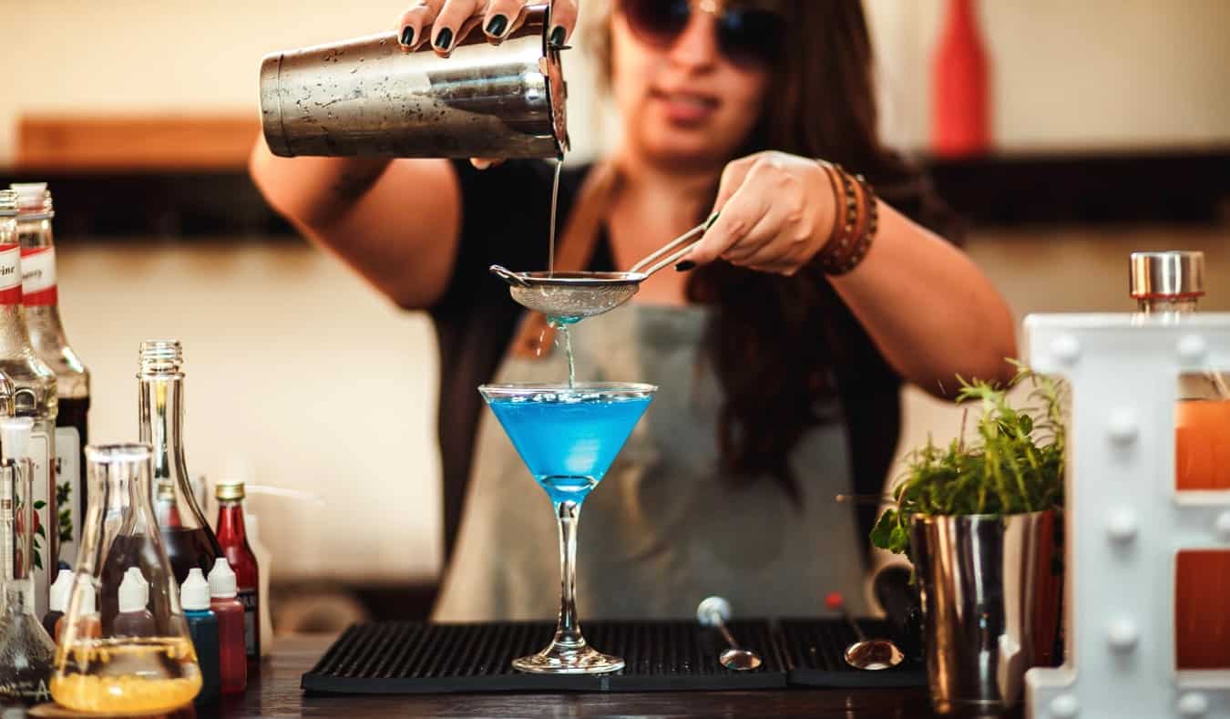 A female bartender pouring a colorful drink at the bar